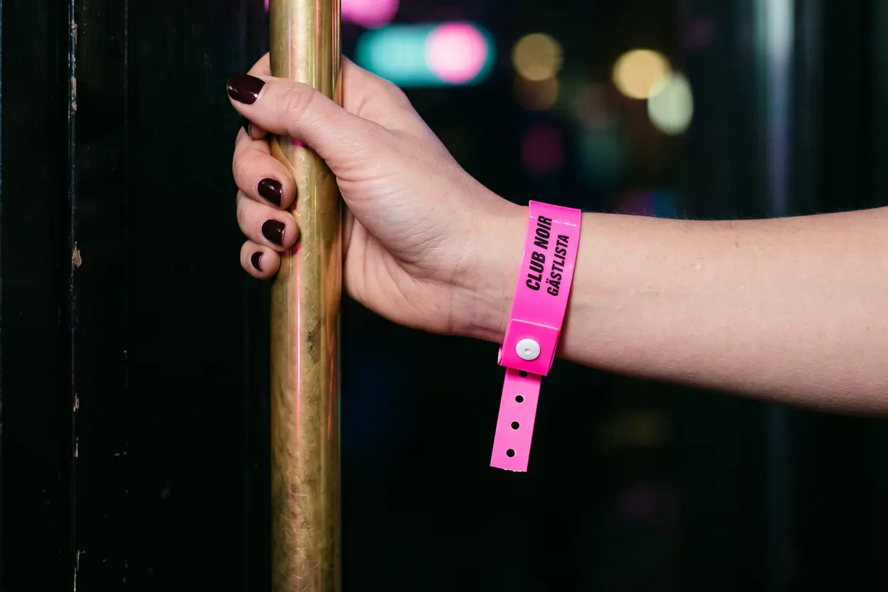 Hand på ett dörrhandtag med ett neonrosa vinylband, CLUB NOIR GÄSTLISTA